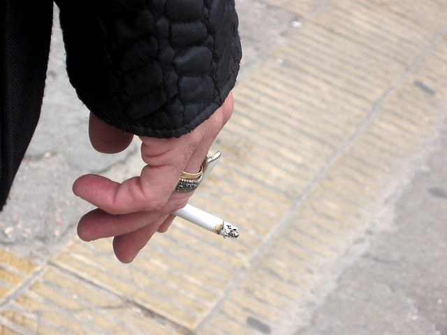 A stock photo of a hand holding a cigarette outside on the street in NYC